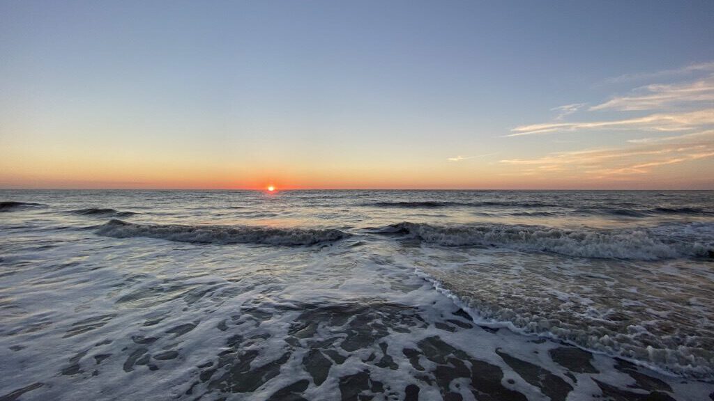 Die Sonne geht unter pastellfarbenem Himmel im Meer auf Baltrum unter
